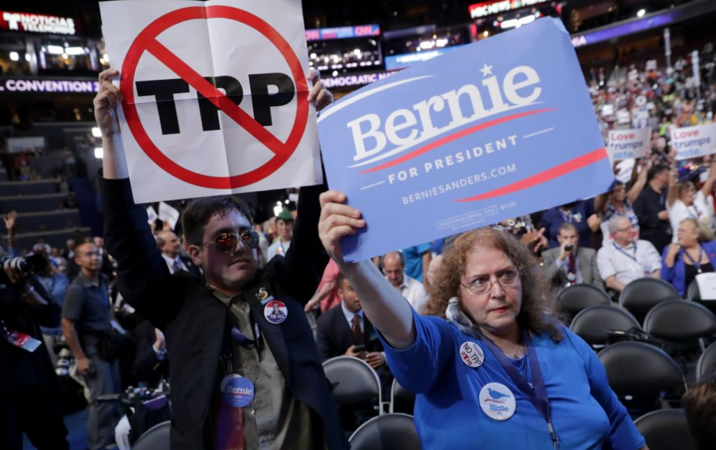 2 people at a rally in the USA hold 'no TPP' and 'Bernie for President' placards.