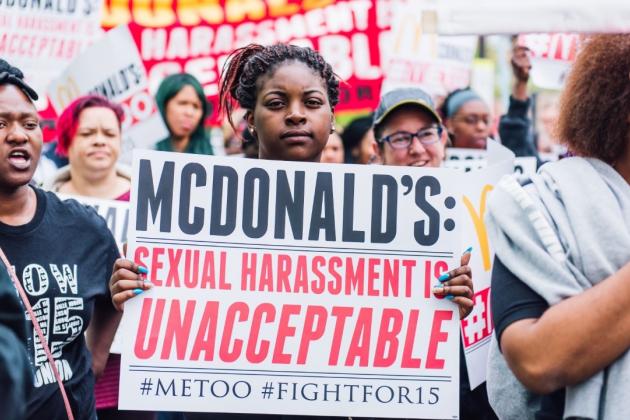 A Black woman at a demonstration faces the camera holding a sign that reads "McDonald's: sexual harassment is unacceptable #MeToo #FightFor15. She has black braids with a red streaks, tied up. Credit: FightFor15 Chicago