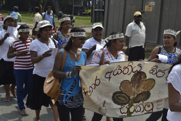People walking through a street protesting. They are holding banners.