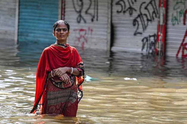 Woman in red outfit wades through flood water up to her thighs