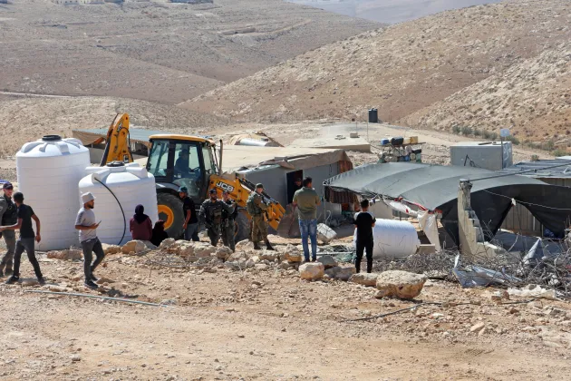 Yellow JCB bulldozer in small settlement with armed forces around