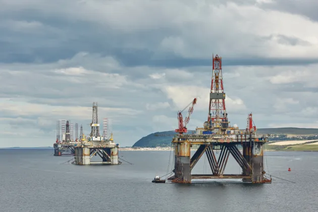 An oil rig drilling platform can be seen in the middle of the sea. There are three structures, with the biggest one in the front. 