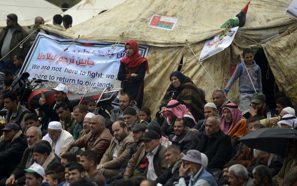 A crowd of Palestinians gather outside a tent at the Great Return March. A banner on the tent reads "We are not here to fight. We are here to return to our lands". Credit: Mohammed Zaanoun/Activestills.org