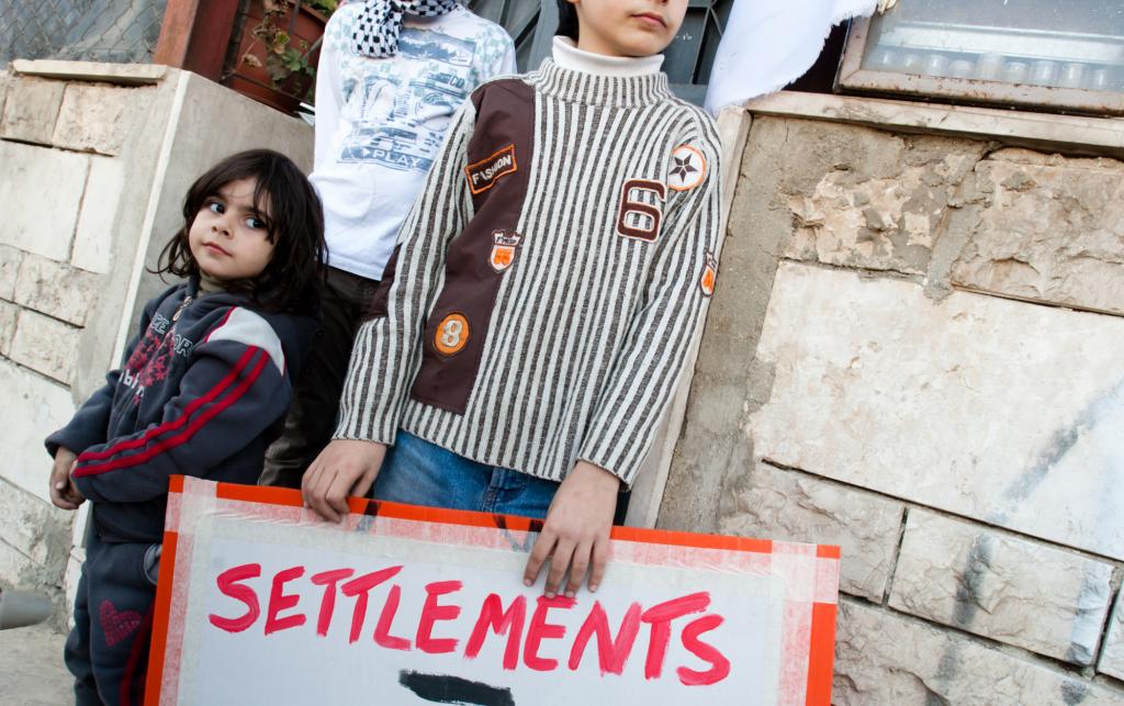 Palestinian children hold a sign that says "Settlements = Obstacle for Peace". Credit: Ryan Rodrick Beiler/ActiveStills 