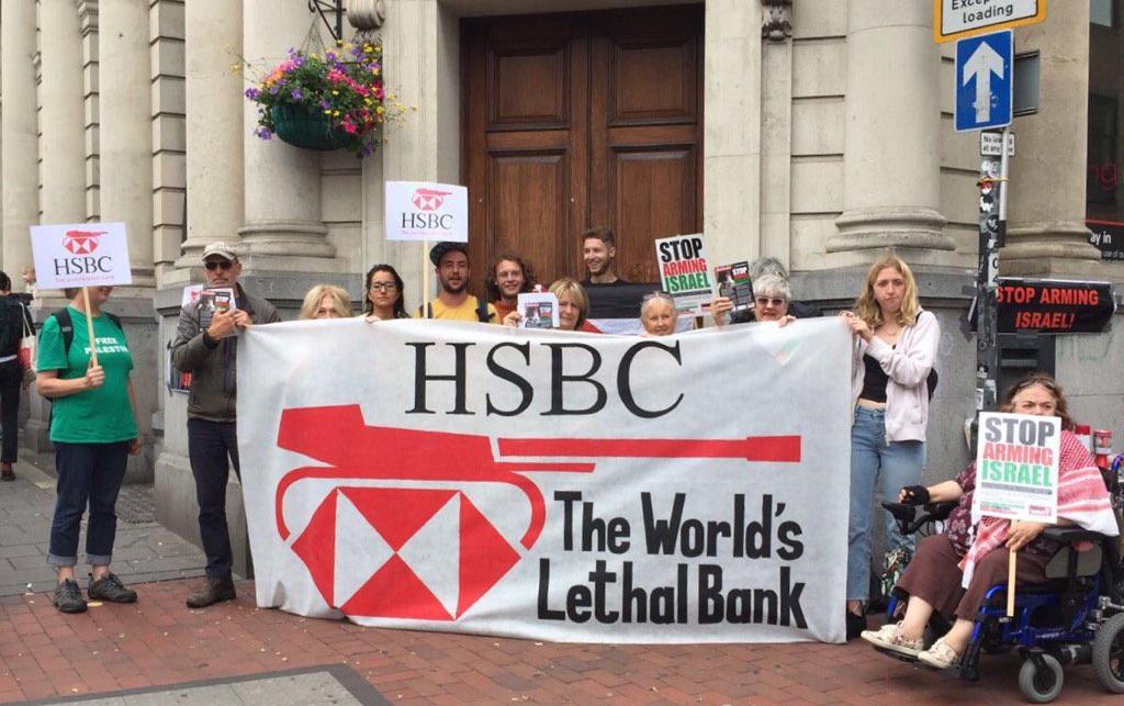 A picket at a HSBC branch in Brighton. Campaigners hold "Stop Arming Israel" placards and a banner that says "HSBC: The World's Lethal Bank", with the HSBC logo made to look like a tank.