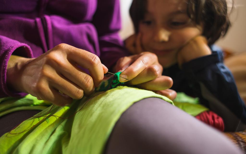 A woman sews a patch on torn clothes from an old sock. 