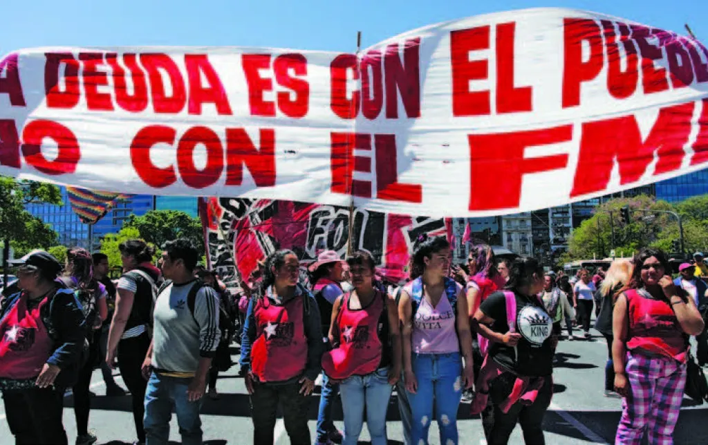 “The debt is with the people. Not with the IMF.” Argentines protest in front of the IMF offices in Buenos Aires in 2019. Previous page: A statue of a Belgian colonialist, daubed in red paint to symbolise the violent legacy of colonialism.