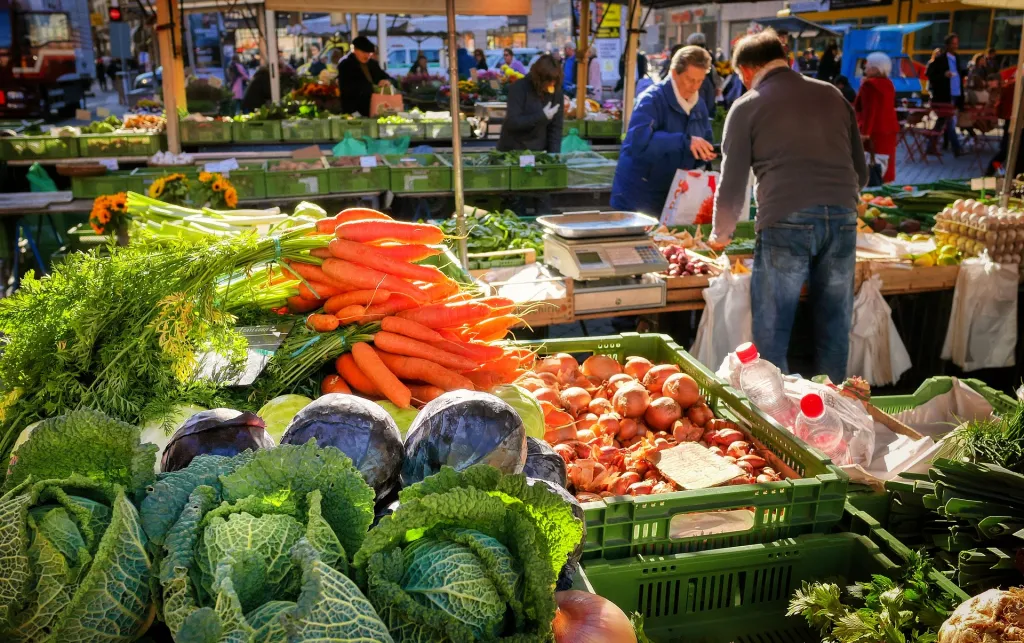 A farmers market where all sorts of vegetables can be seen including carrots, onions, cabbages.