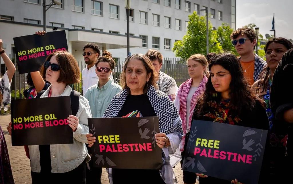 People at a protest holding signs saying 'No more oil, no more blood' and 'Free Palestine'