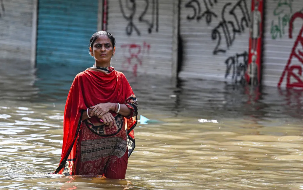 Woman in red outfit wades through flood water up to her thighs
