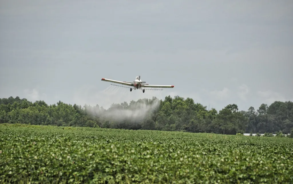 Airplane spraying pesticides over land with bright green plants