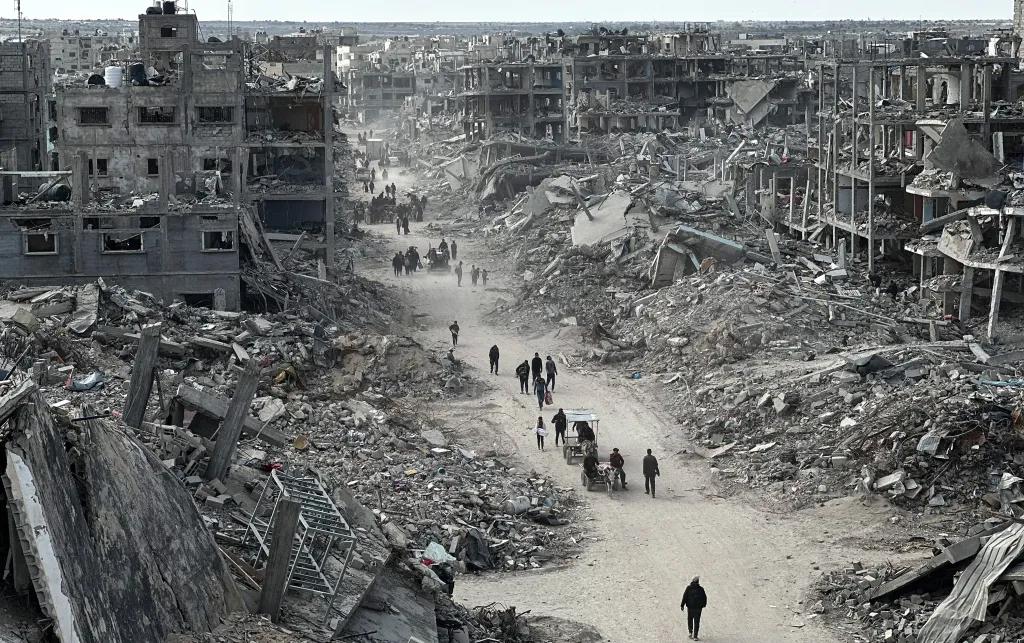 People walk along a path, surrounded by destroyed buildings