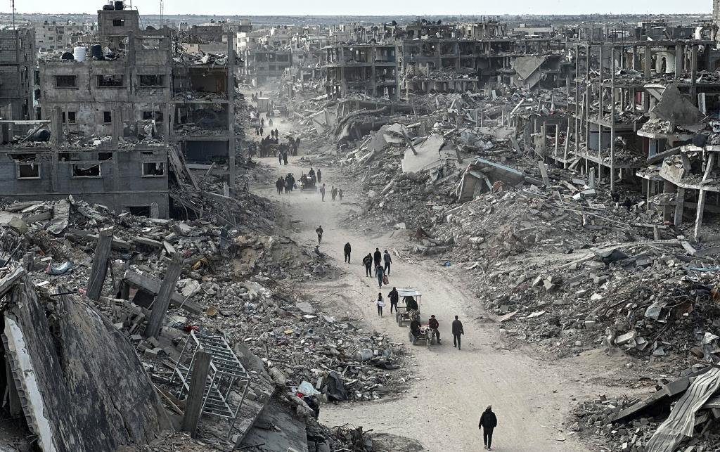 People walk along a path, surrounded by destroyed buildings