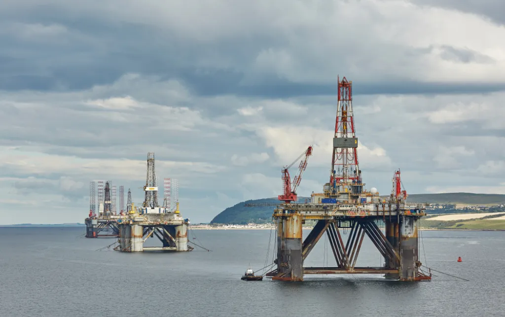 An oil rig drilling platform can be seen in the middle of the sea. There are three structures, with the biggest one in the front. 