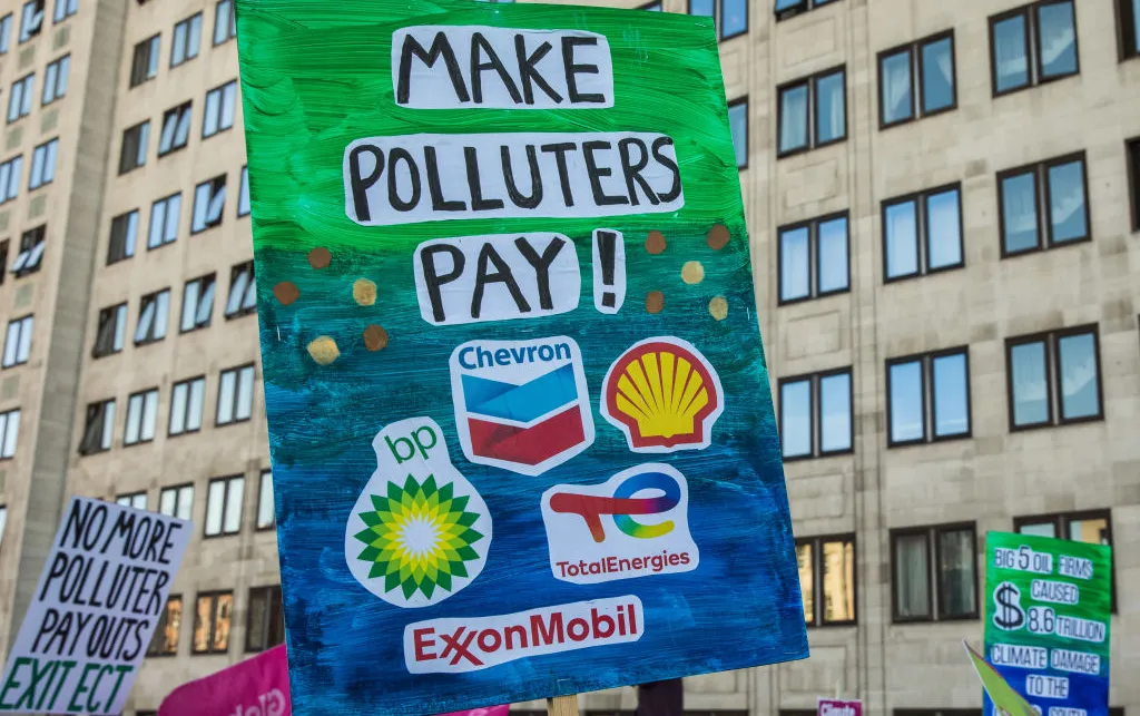 A sign with logos of fossil fuel corporations such as Shell and BP on it. It also has the words 'Make Polluters Pay!' written on it.