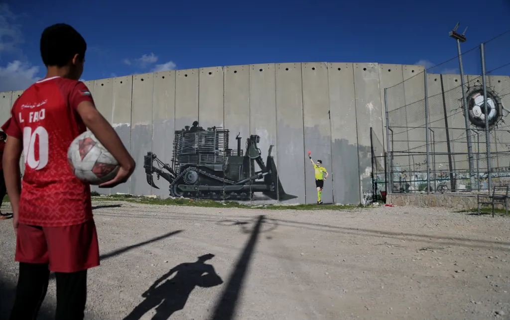 Boy holds football and looks at graffiti 