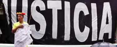 An indigenous man with stands in front of a giant banner that says "Justicia"