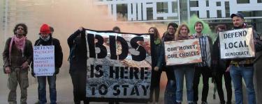 Campaigners hold placards and banners that read: "Defend the right to demonstrate against apartheid – Join this movement"; "BDS is here to stay"; Our money, our choices"; "Defend Local Democracy". Credit: London Palestine Action