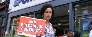 A protestor holds a placard that says 'End Precarious Contracts' outside of a Sports Direct store in Hackney. Credit: War on Want.