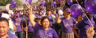 Women workers who are members of Codemuh take part in a street demonstration, wearing purple and holding purple balloons.