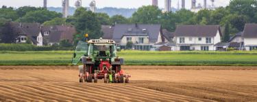 A tractor in a field, with houses and chimneys in the background. Thomas B. from Pixabay