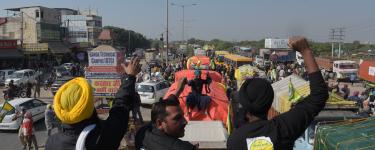 Farmers protest in Delhi, sitting on a truck with fists raised in the air.