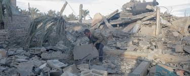 Man surrounded by rubble in the Gaza Strip, bending down to move a piece with his hands