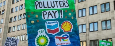 A sign with logos of fossil fuel corporations such as Shell and BP on it. It also has the words 'Make Polluters Pay!' written on it.