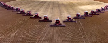 A field with lots of tractors lined up on it. The sky looks grey with dark clouds.
