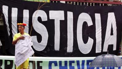 An indigenous man with stands in front of a giant banner that says "Justicia"