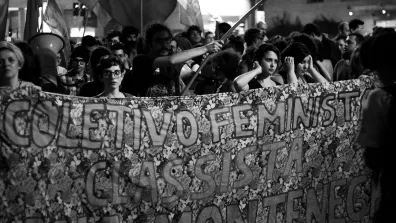 Black and white photo of Brazilian protestors holding a banner that says "Coletivo Feminista Classista Ana Montenegro". Photo: fabio montarroios CC BY 2.0