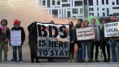 Campaigners hold placards and banners that read: "Defend the right to demonstrate against apartheid – Join this movement"; "BDS is here to stay"; Our money, our choices"; "Defend Local Democracy". Credit: London Palestine Action