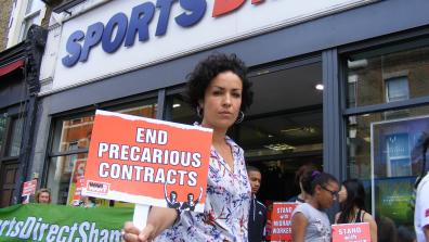 A protestor holds a placard that says 'End Precarious Contracts' outside of a Sports Direct store in Hackney. Credit: War on Want.
