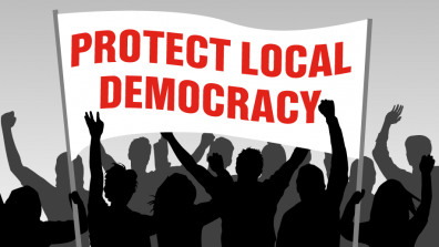 An illustration of a crowd in black and grey, holding up a white banner with red type that reads 'PROTECT LOCAL DEMOCRACY'.