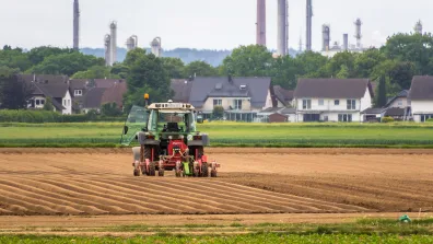 A tractor in a field, with houses and chimneys in the background. Thomas B. from Pixabay