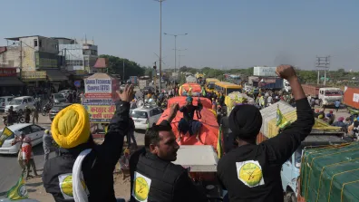 Farmers protest in Delhi, sitting on a truck with fists raised in the air.