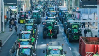 Three rows of green tractors make their way through a busy high street during a protest.